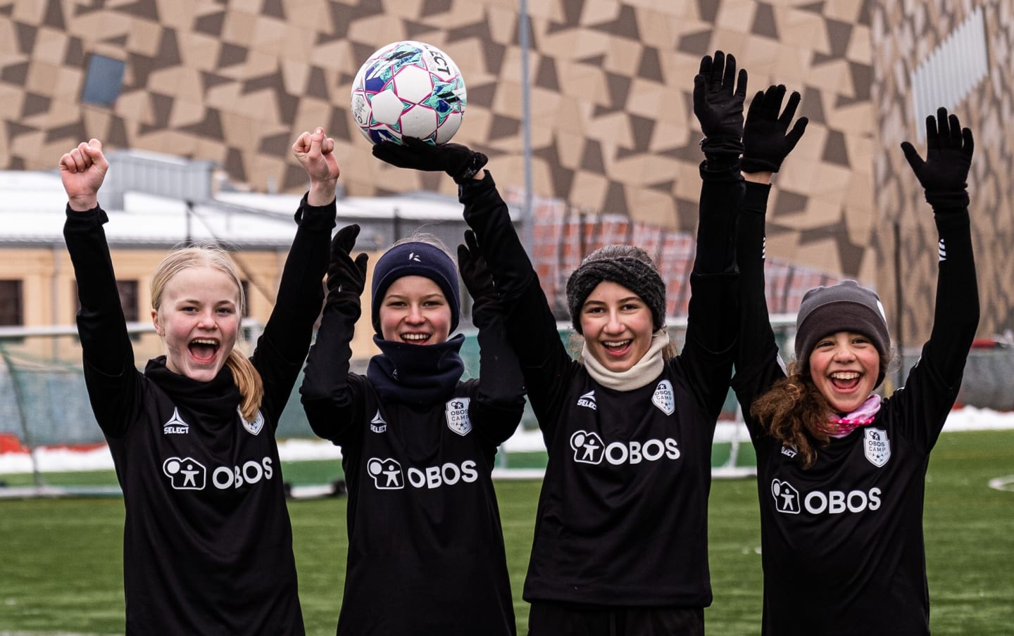 Fire fotballjenter står ved siden av hverandre og jubler med hendene i været. Hun ene holder en fotball i ene hånda.