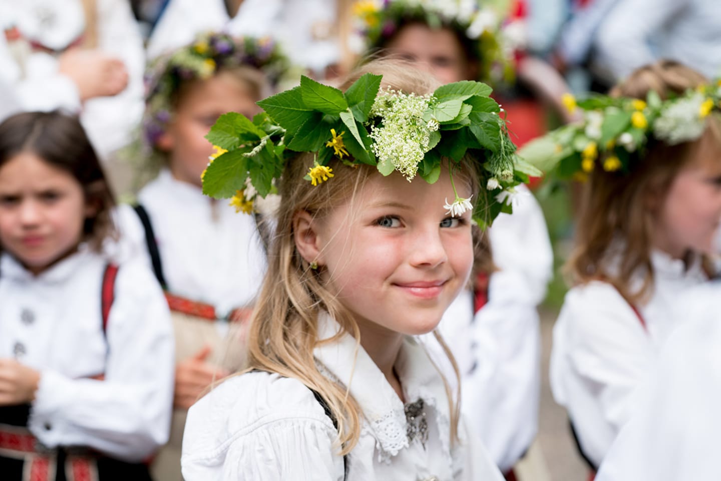 Foto av en liten jente som smiler til kameraet med en grønn og gul blomsterkrans på hodet.