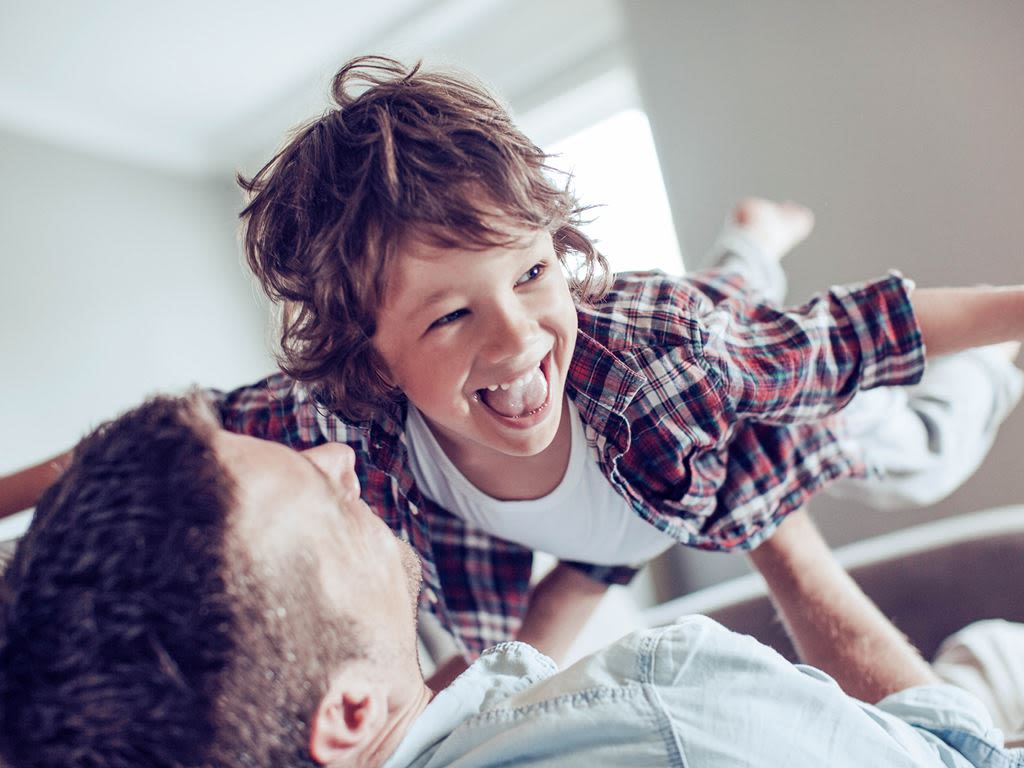 Pappa ligger i sängen med son som leker flygplan 