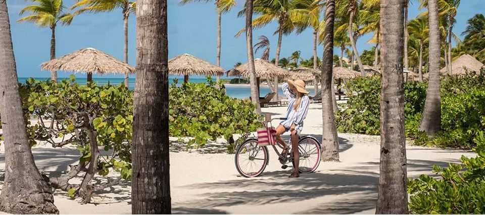 Woman cycling along the beach, Jumby Bay Island Antigua