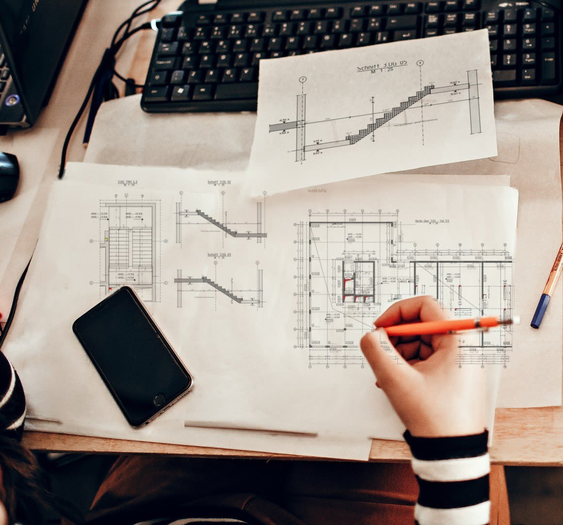 A drafter marking up structural plans, a stair section and a floor plan, next to the keyboard