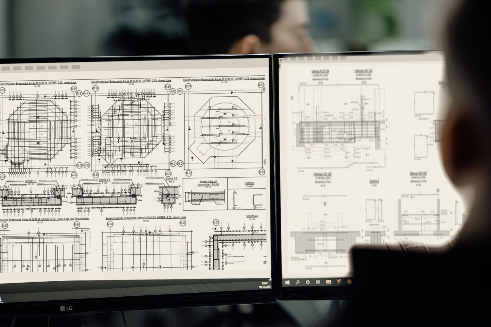 A drafter reviewing reinforcement plans on two monitors