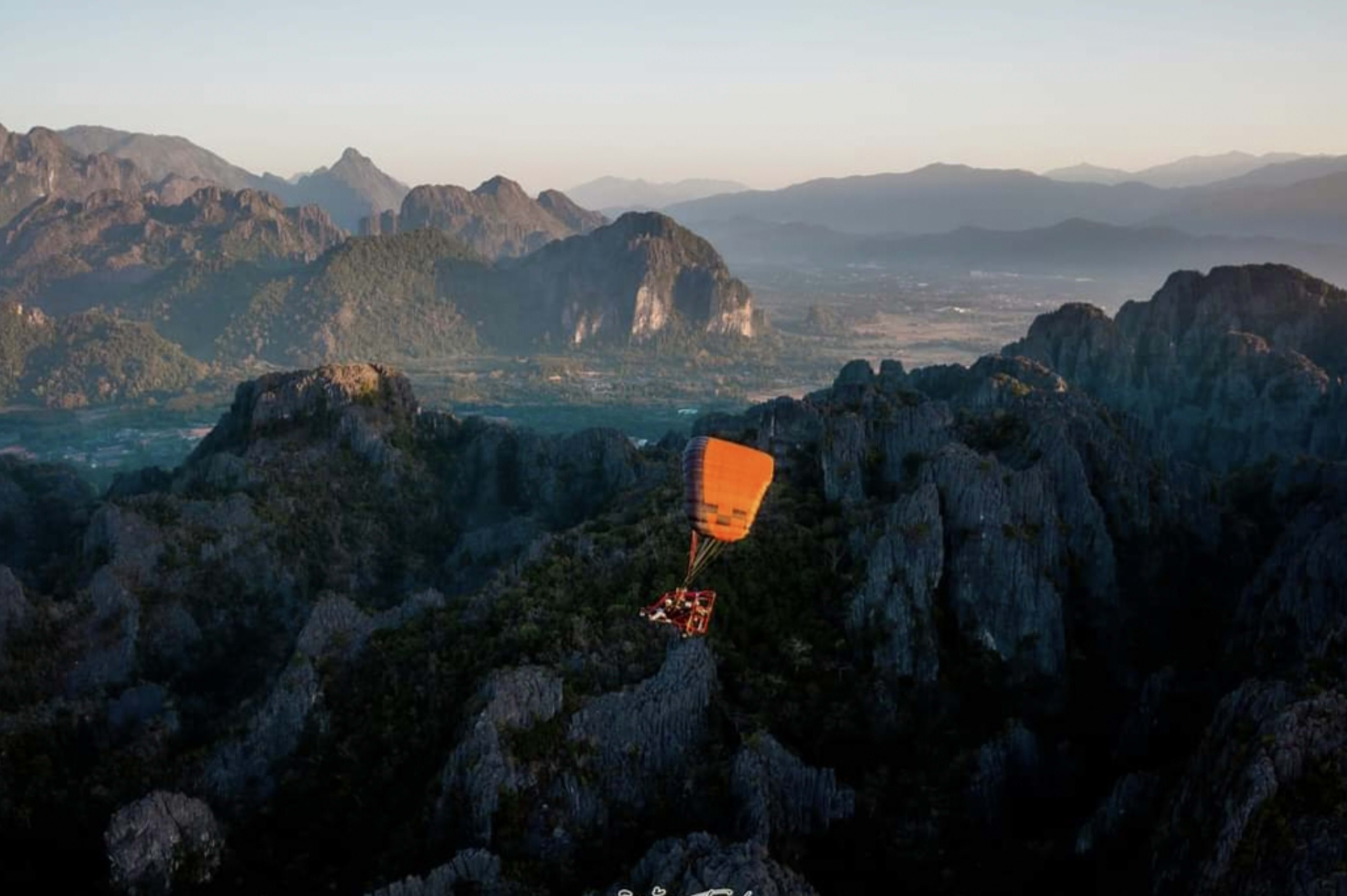 Powered paraglider soaring above Vang Vieng limestone karsts at sunrise