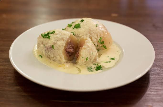 Cepelinai stuffed with pork and served with sour cream