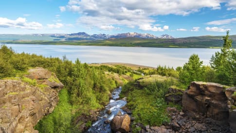 Water course falling down to Lagarfljot lake in Eastern Iceland, the mountain landscape of Fljotsdalsherad municipality is at background