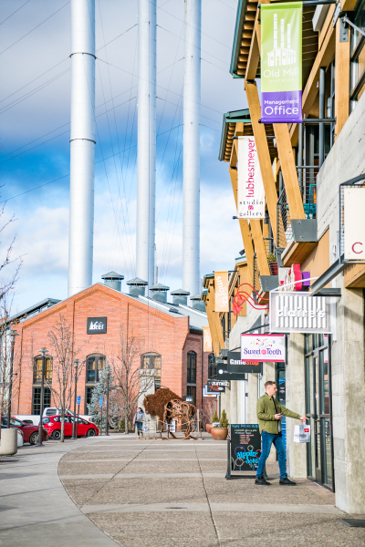 A man is walking down a sidewalk in front of a building with a cow in the background.