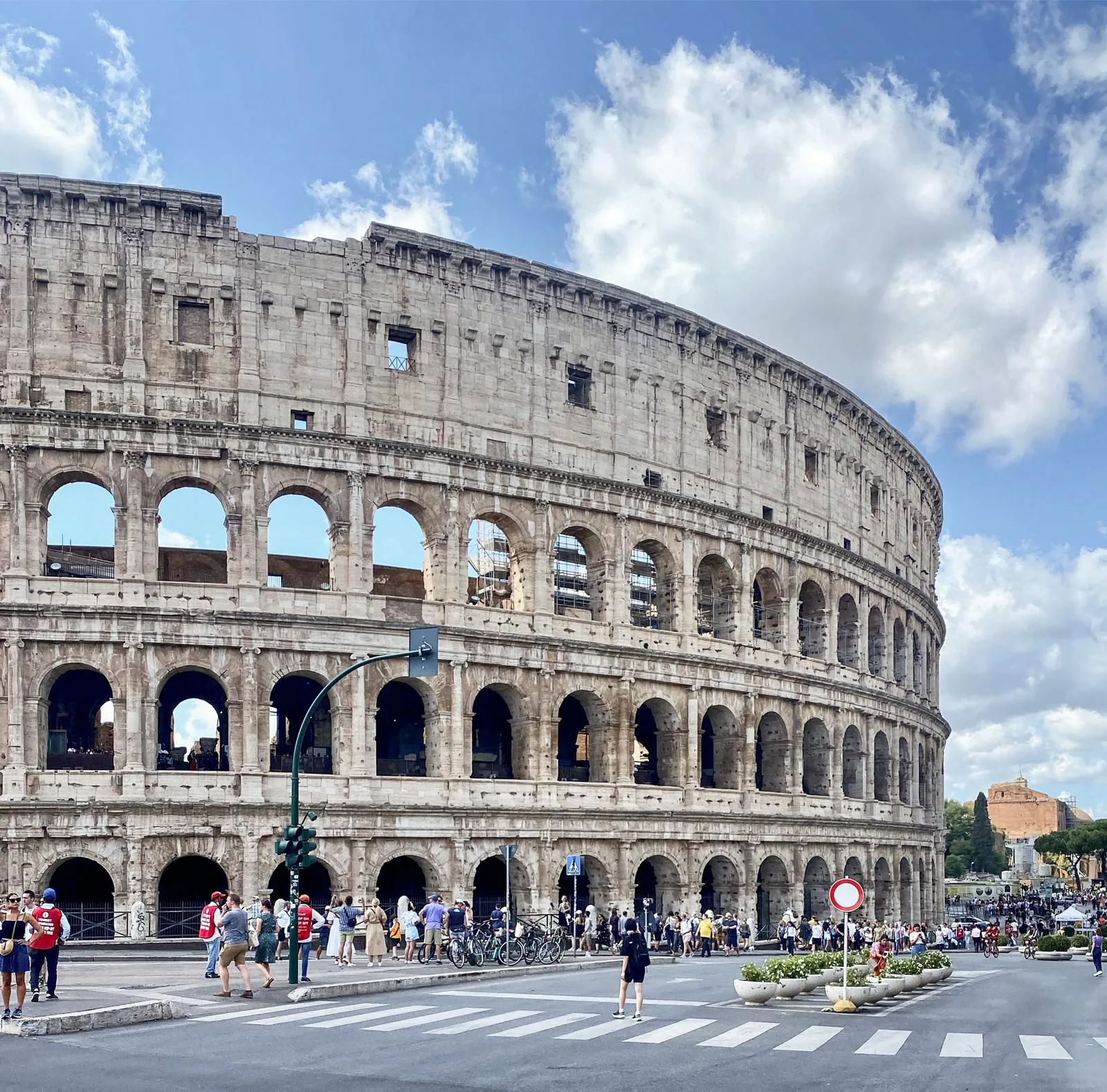 The Colosseum under a bright sky with crowds along the street