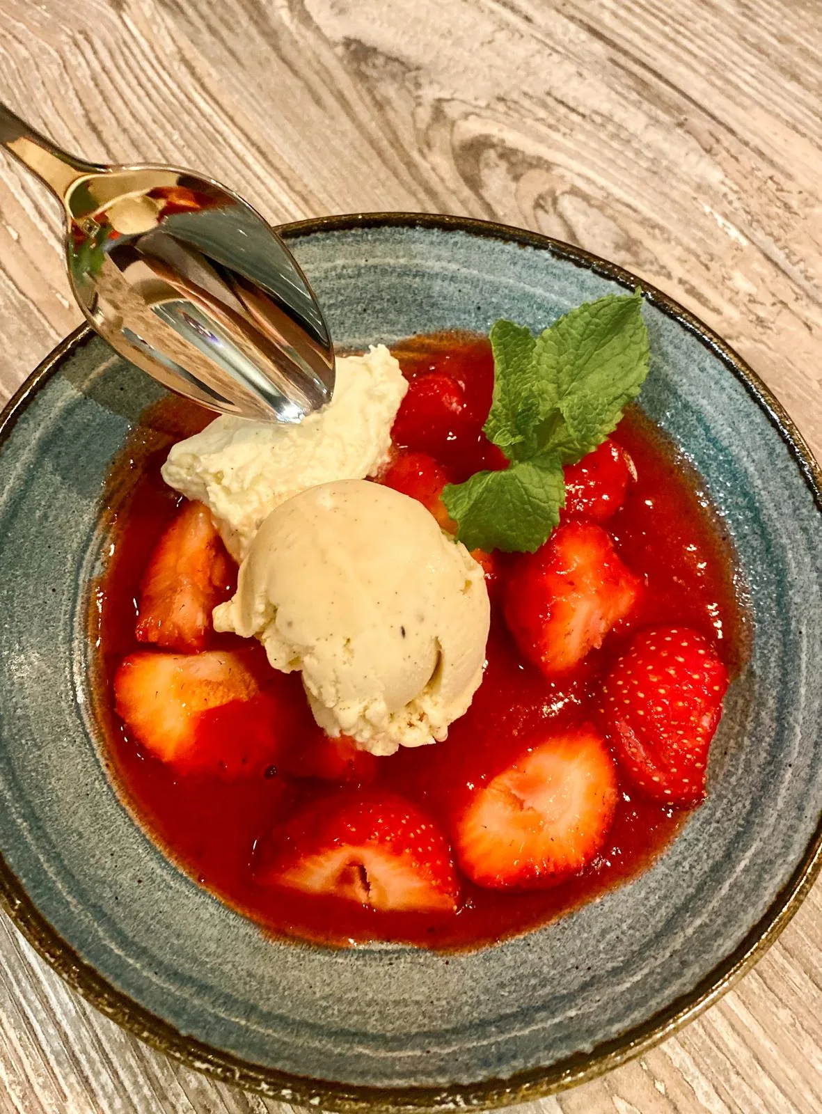 Strawberries in syrup topped with a scoop of gelato and mint, in a ceramic bowl