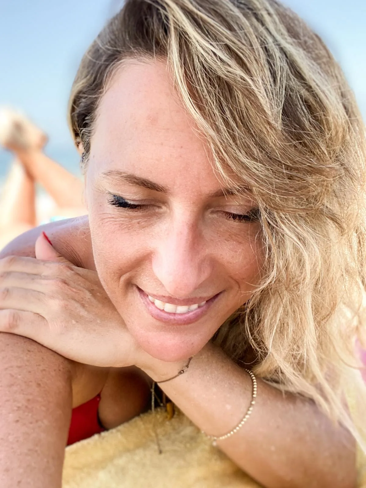 A close portrait of Elinor smiling, resting on a towel on a sunlit beach