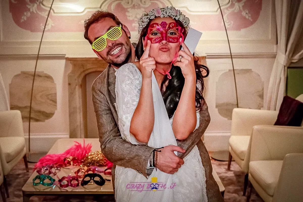 Gli sposi con maschera e occhiali da festa accanto al tavolo degli accessori, Hotel Monaco di Venezia