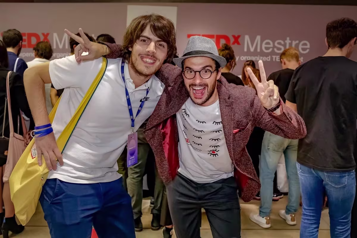 Due partecipanti del TEDx Mestre fanno il segno di vittoria davanti al fondale dell’evento