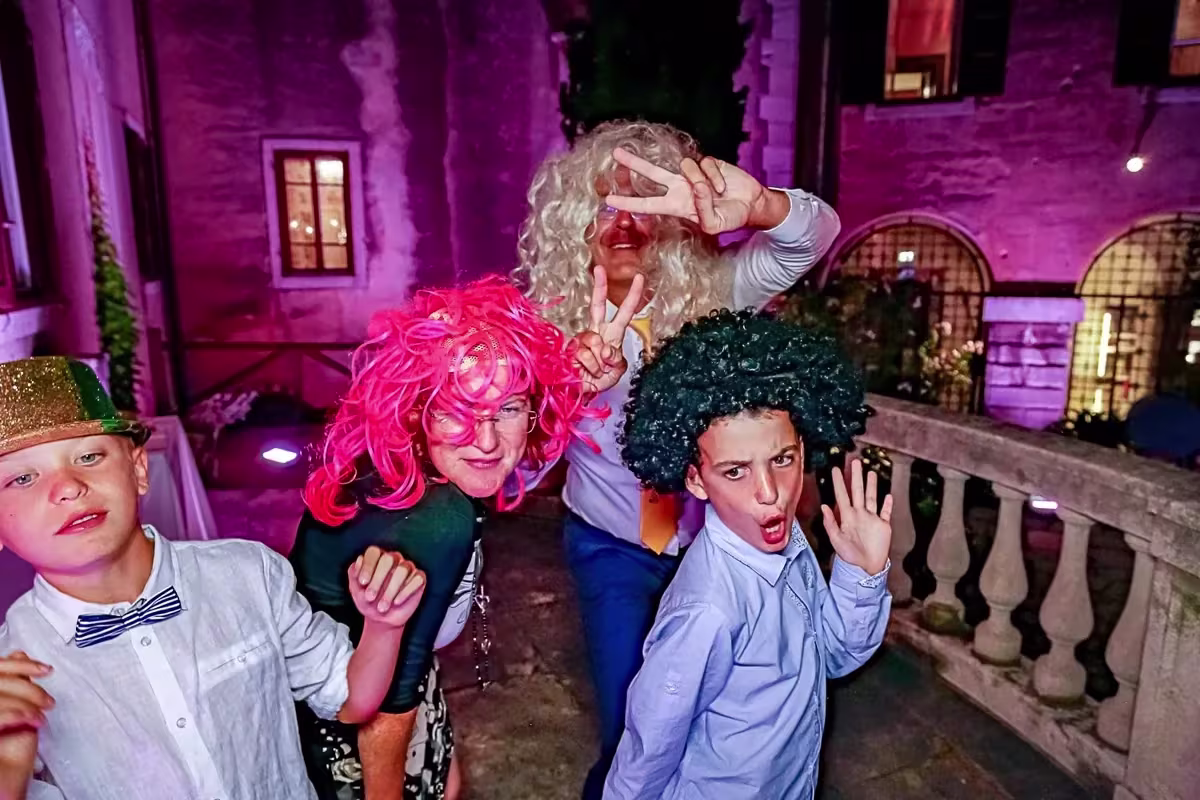 Ragazzi con parrucche colorate e cappelli nel cortile illuminato del Castello di Duino