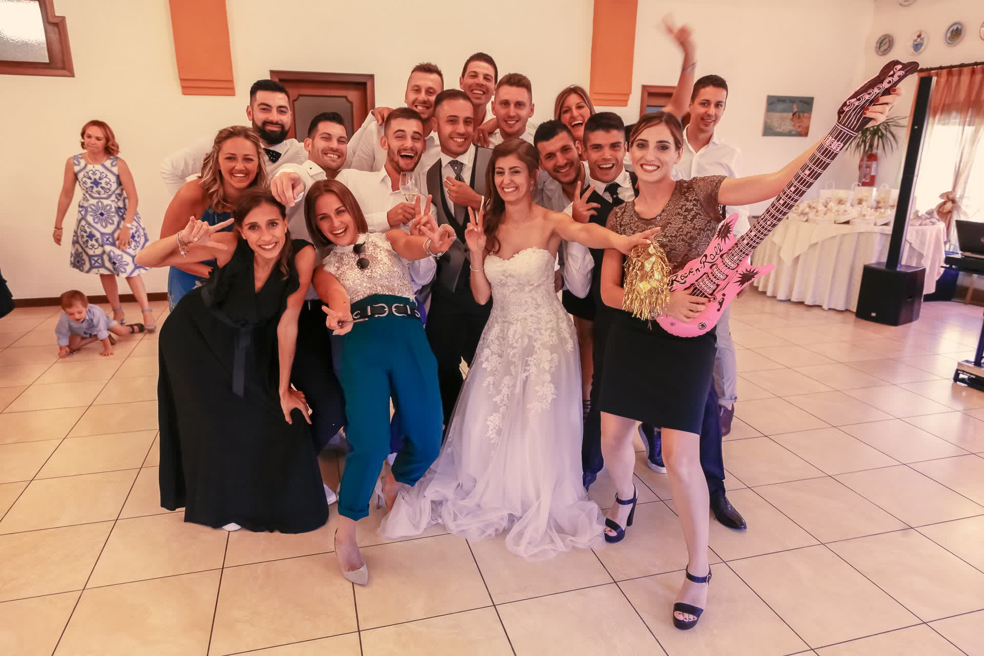 La sposa e un gruppo numeroso di invitati ammassati davanti alla cabina, con una chitarra gonfiabile