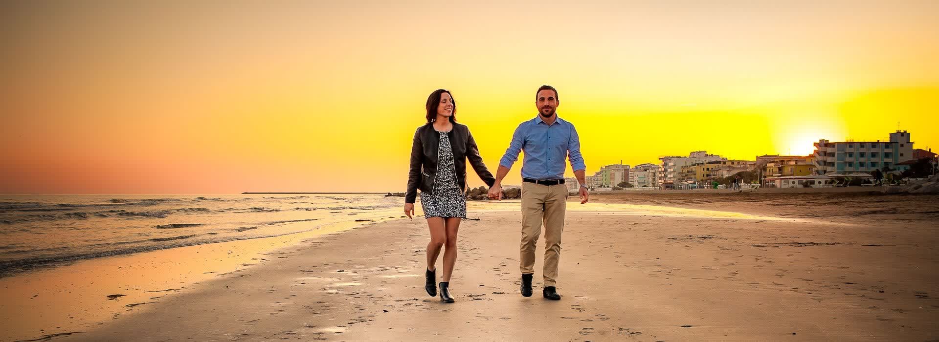 A couple walking hand in hand along the shoreline, the low sun behind them