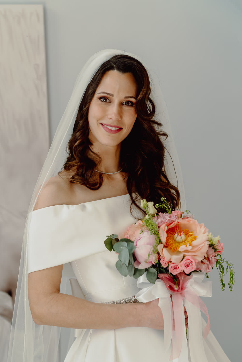 The bride holding her peony bouquet in the soft light of a white room