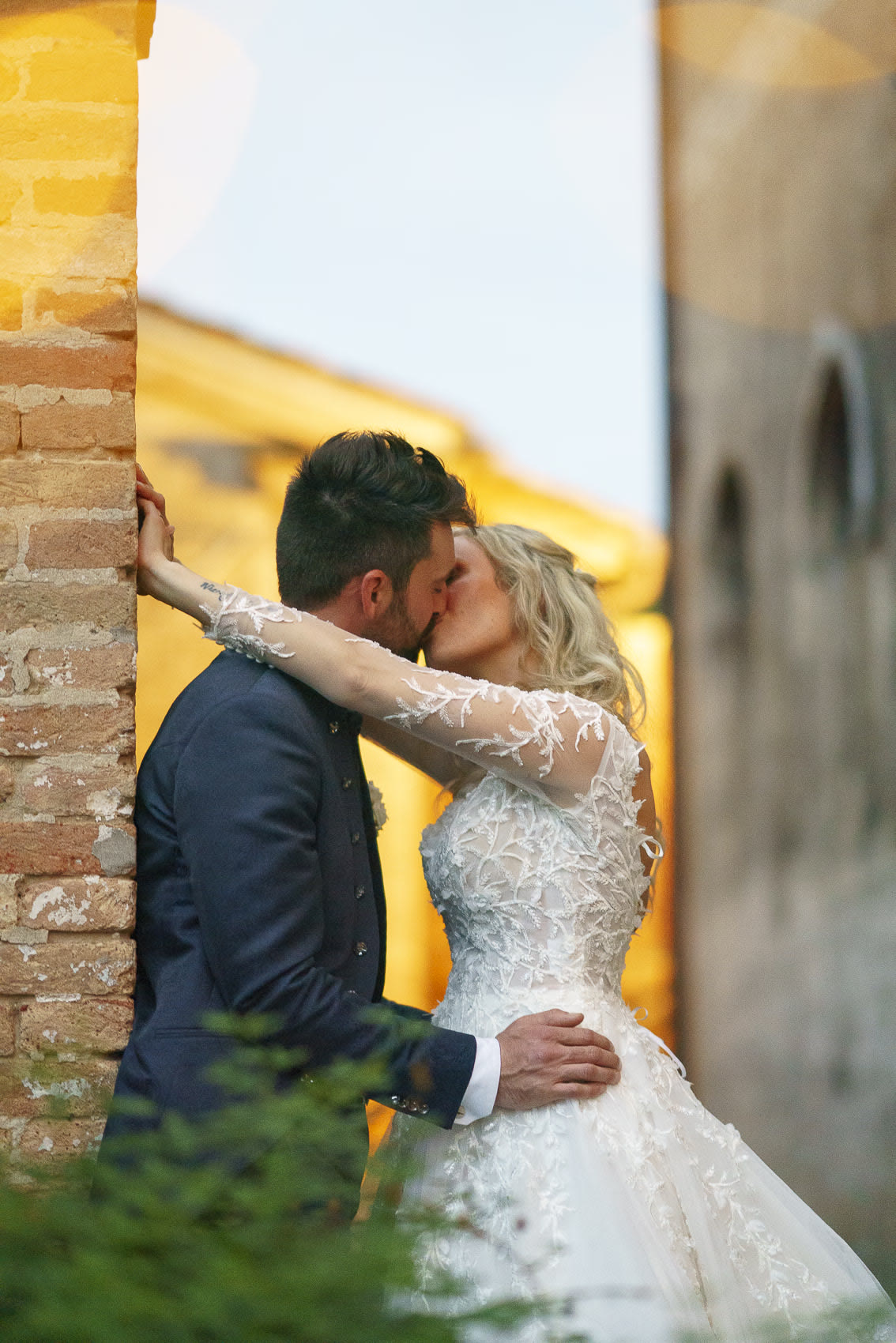 The couple kissing against a brick wall in the warm evening light