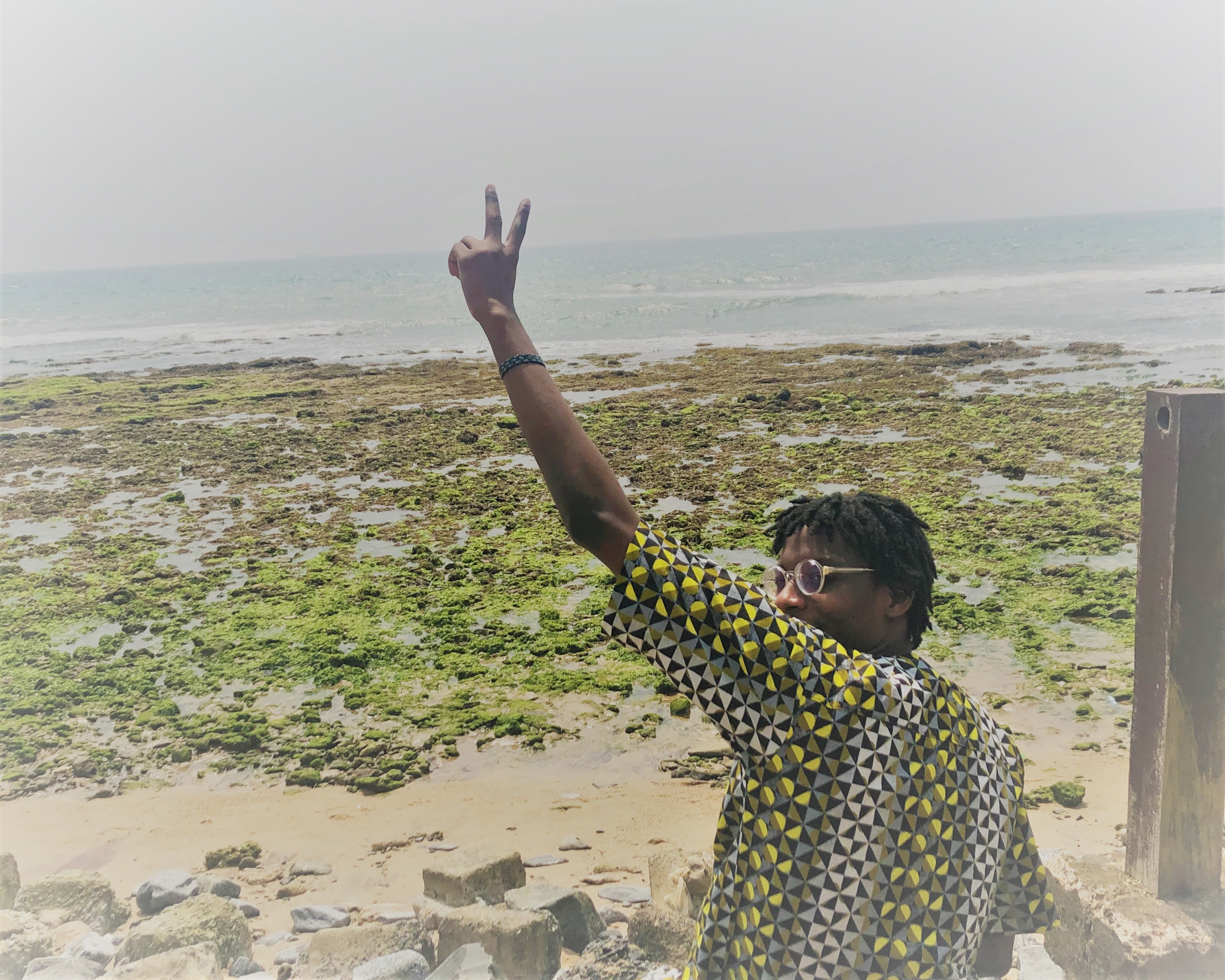 Ore Ogundipe sitting at the beach, throwing a peace sign