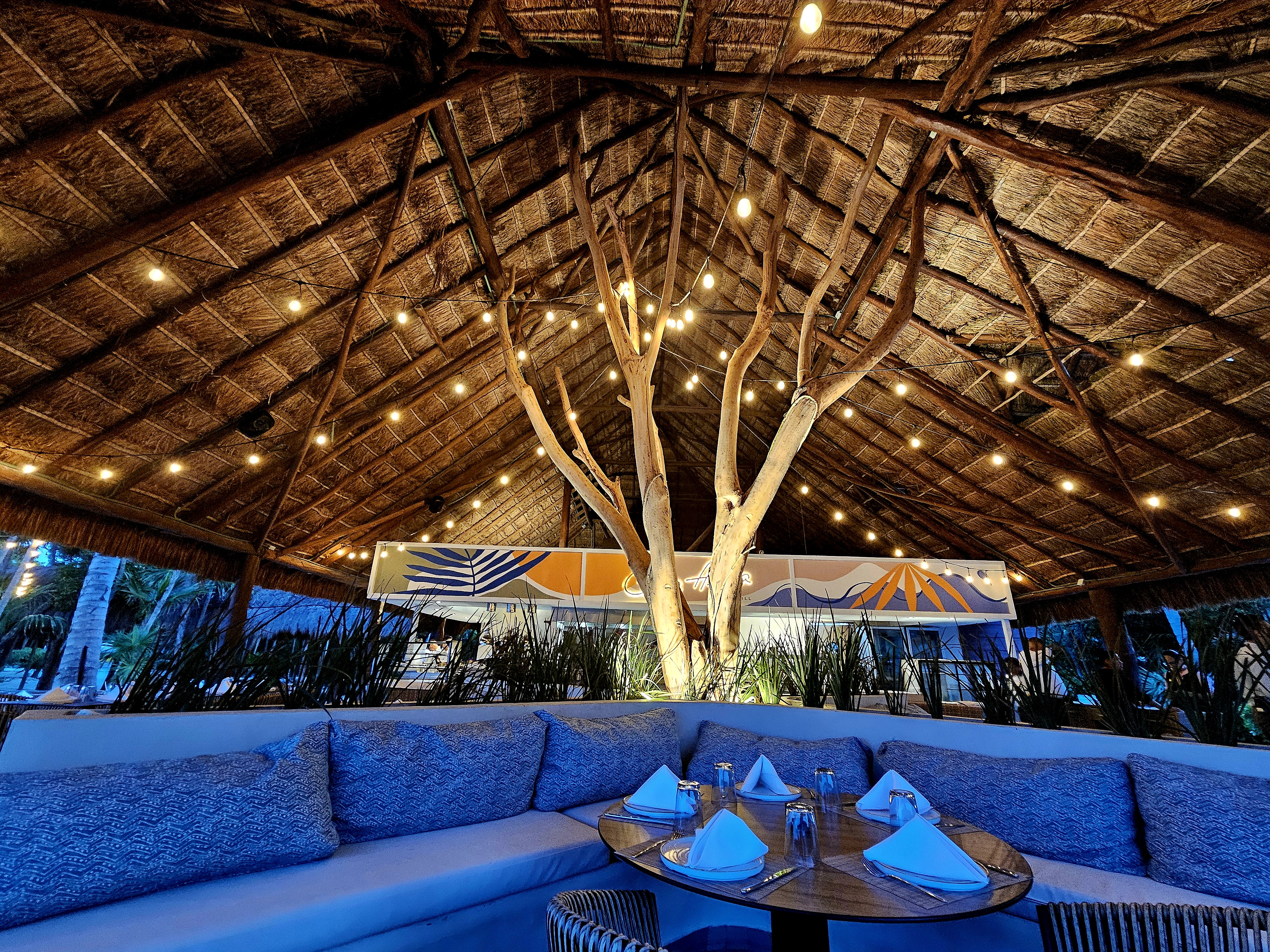 Open-air beachside restaurant with thatched palm roof and string lights