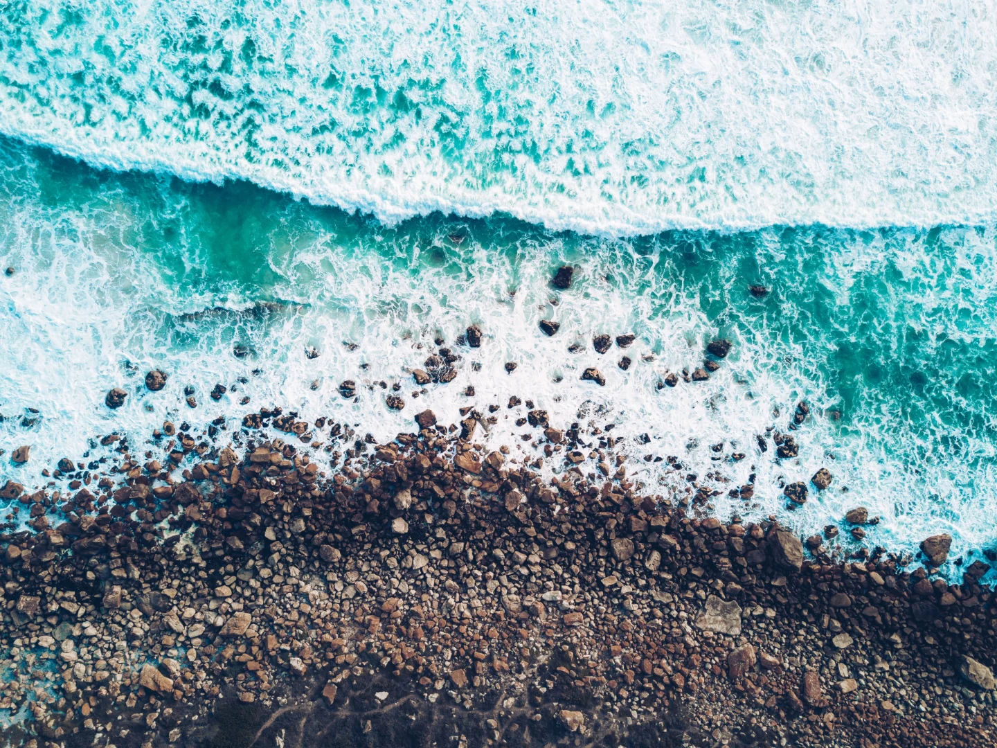 An image of waves hitting the stoney edge of a beach by @johnonolan on unsplash.