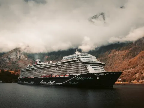 An image of a ship cruising on a river beside a mountain on a cloudy day by @redcharlie on unsplash.