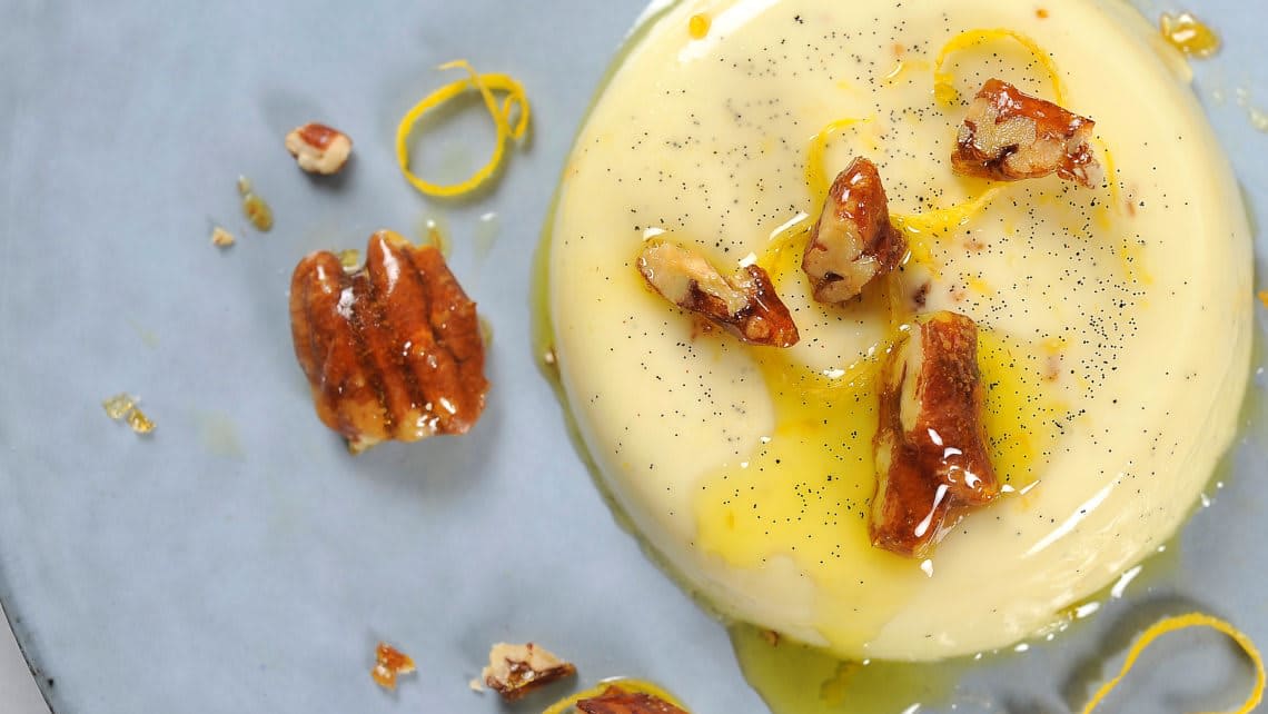 Panna cotta dandert på et fat med olivenolje, pekannøtter og sitronskall.