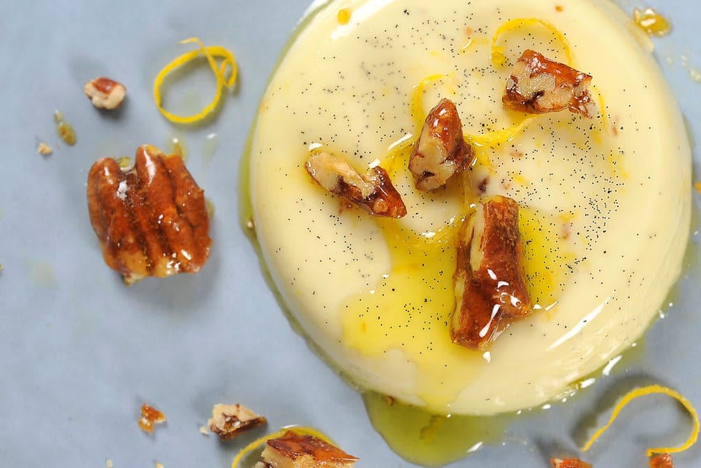 Panna cotta dandert på et fat med olivenolje, pekannøtter og sitronskall.