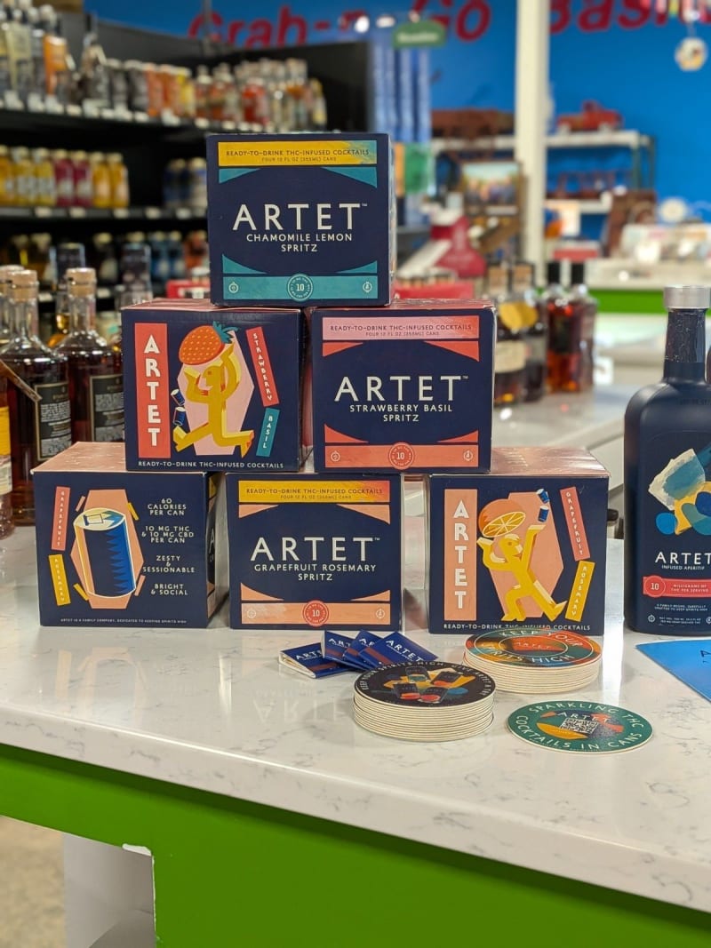 Artet ready-to-drink THC spritz four-packs stacked on a store counter next to the Artet aperitif bottle
