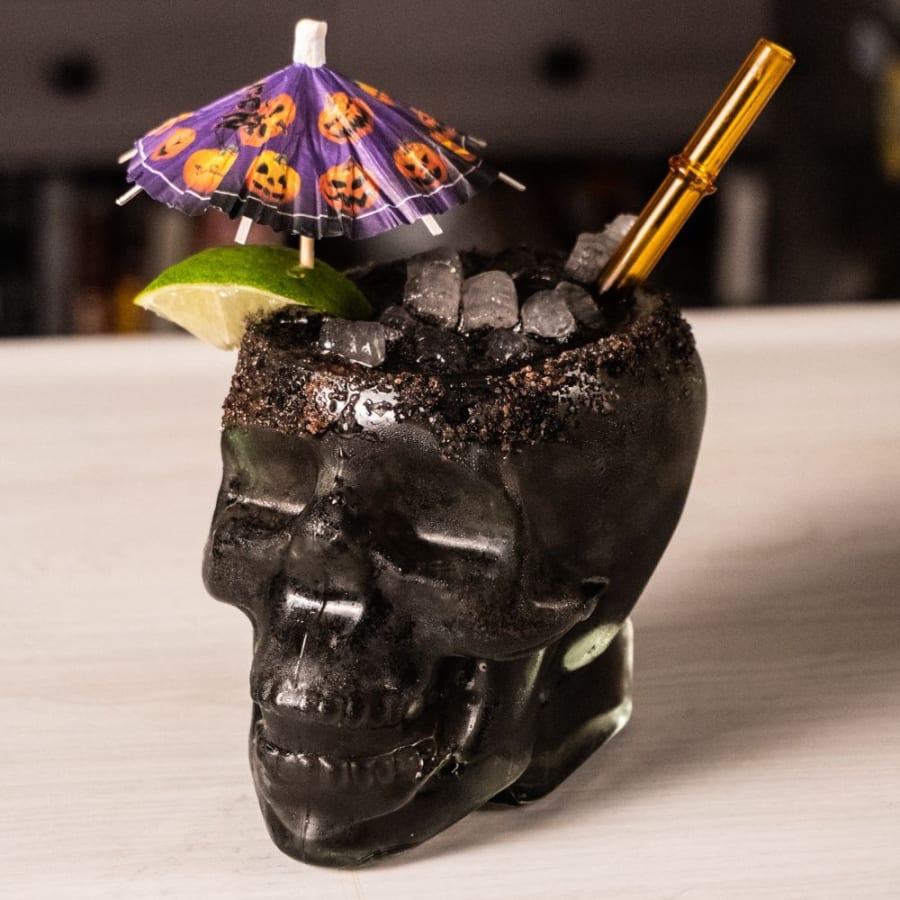 A black margarita in a skull glass with a black lava salt rim