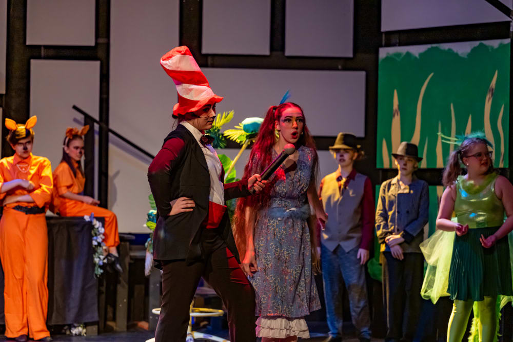 Actors portray the Cat in the Hat interviewing Gertrude McFuzz in front of perturbed Jungle Citizens
