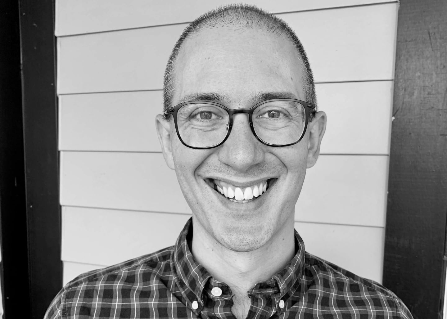 A man wearing glasses and smiling into the camera from two feet away.