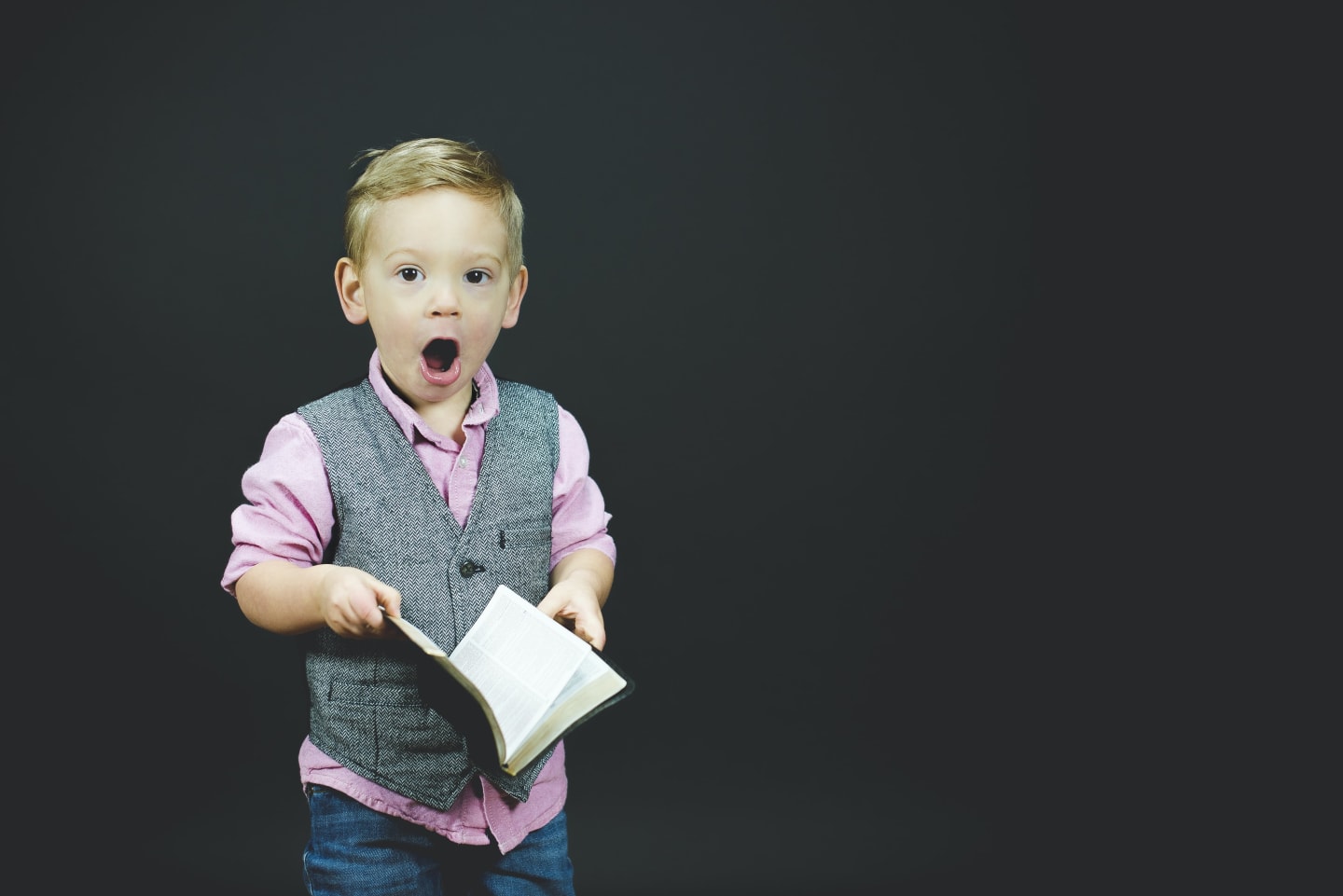 A small boy with his mouth open in surprise while holding a large book.