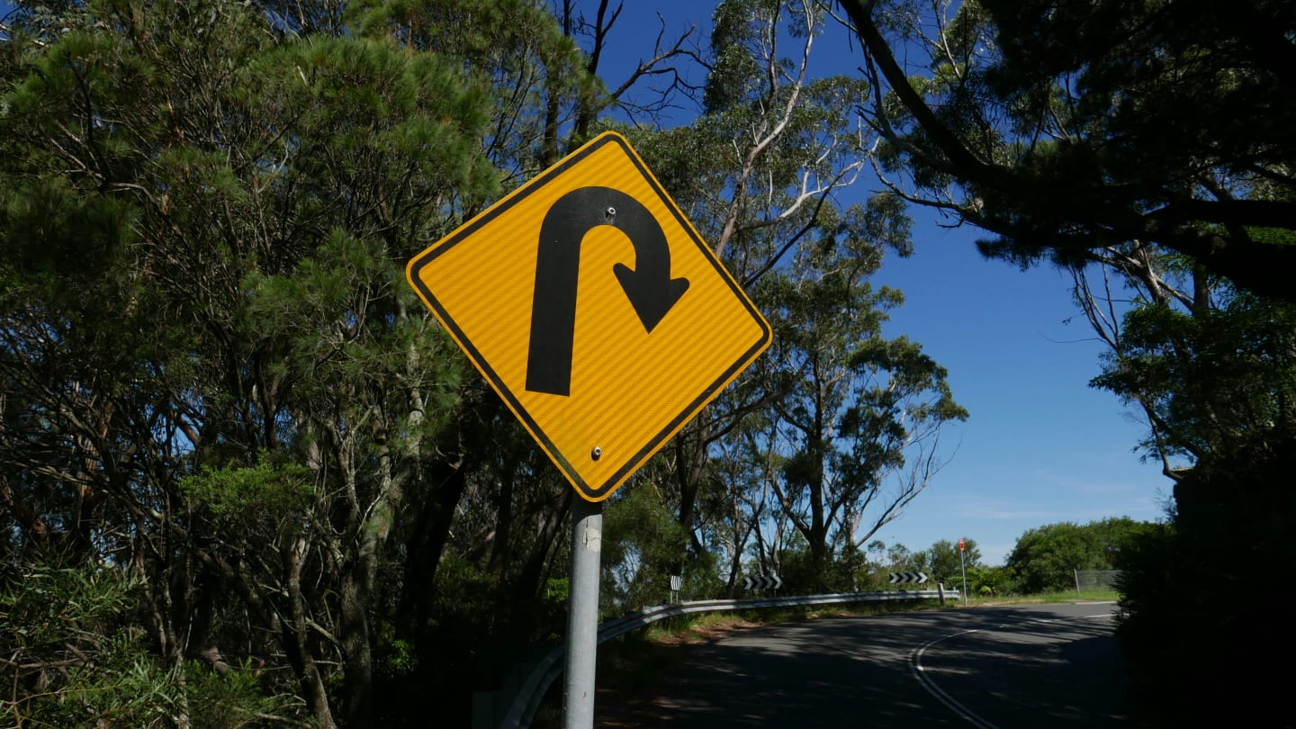 A yellow roadsign showing a 180-degree curve approach, indicating you'll be heading back the way you came.