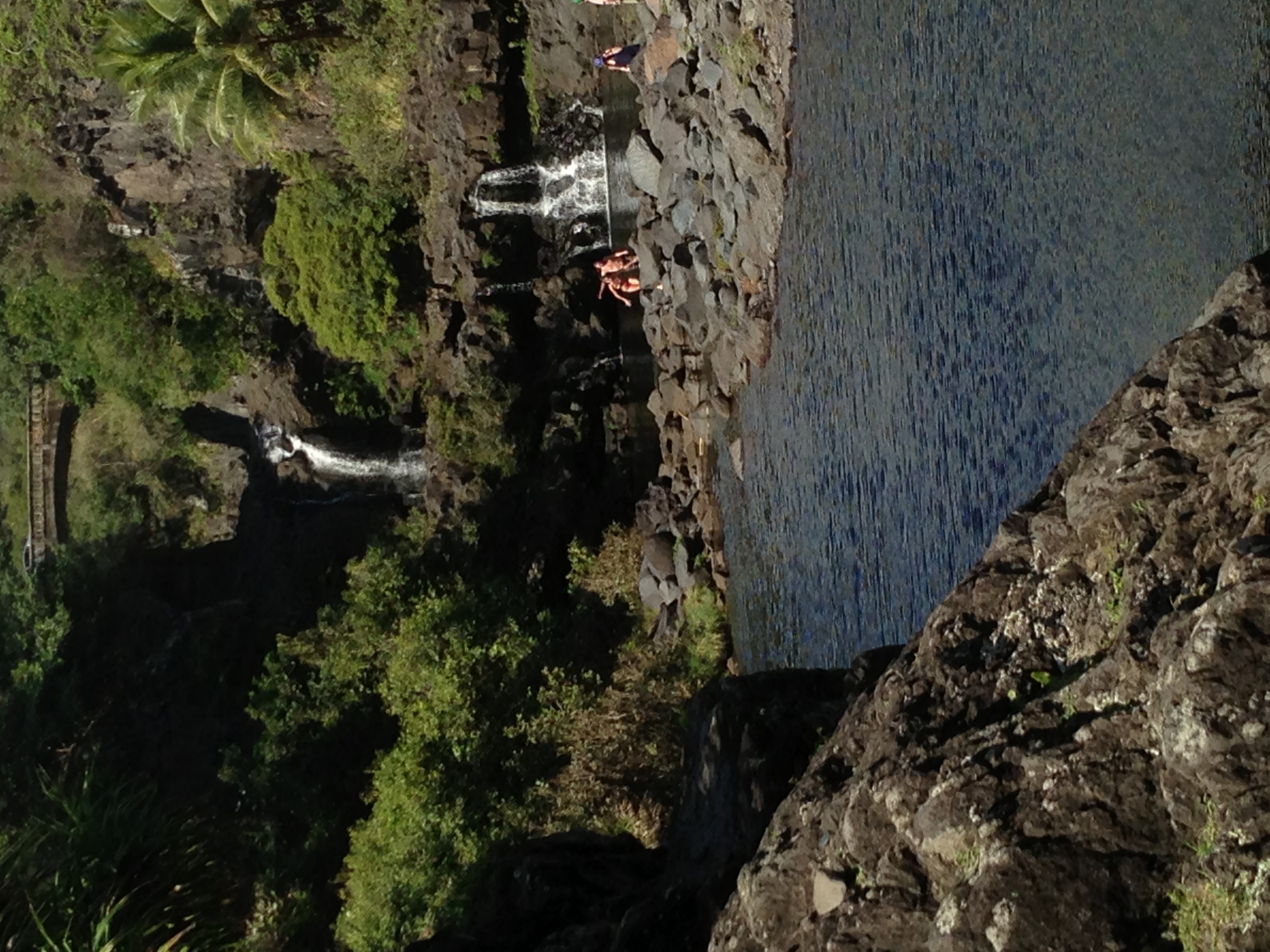 Ohe'o Gulch (Seven Sacred Pools) at Kipahulu — tiered lava pools and waterfall cascading between dark basalt rocks, visitors on the rocks, ocean visible in the background