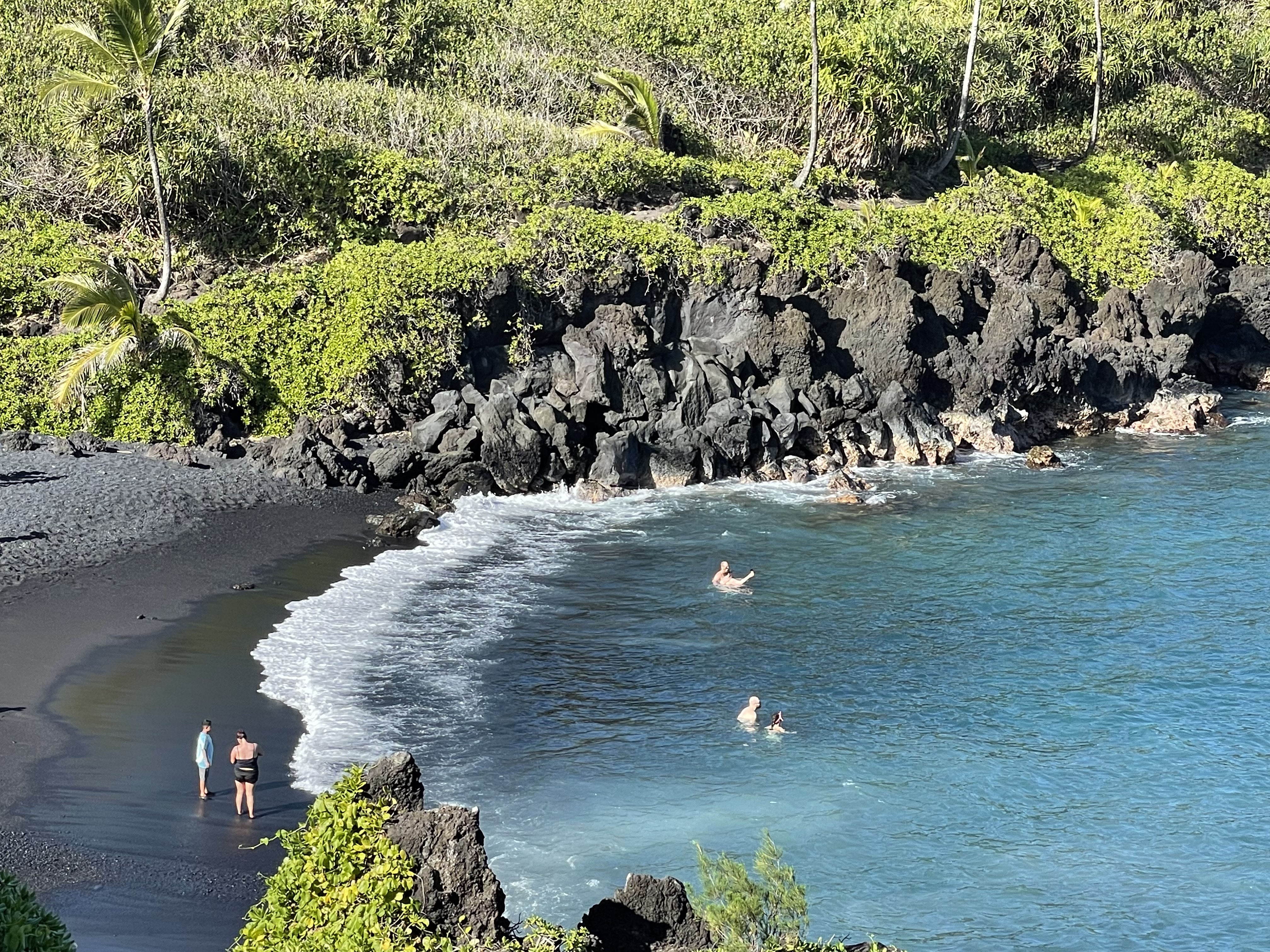 Waiʻānapanapa Black Sand Beach near Hana — swimmers in turquoise water, black lava shoreline