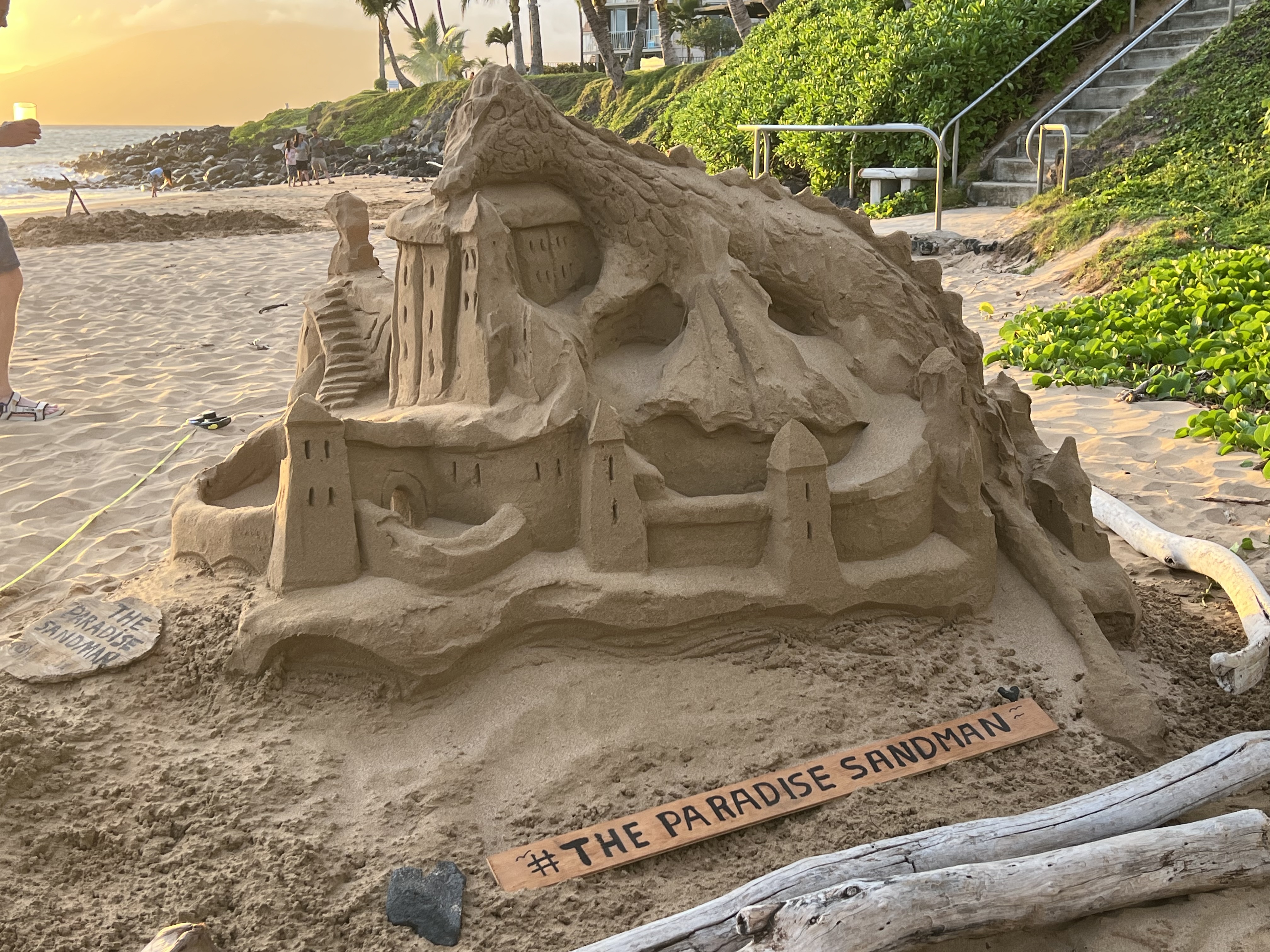 Paradise Sandman castle at sunset — full sculpture with golden sky and West Maui mountains behind, June 29, 2026 evening