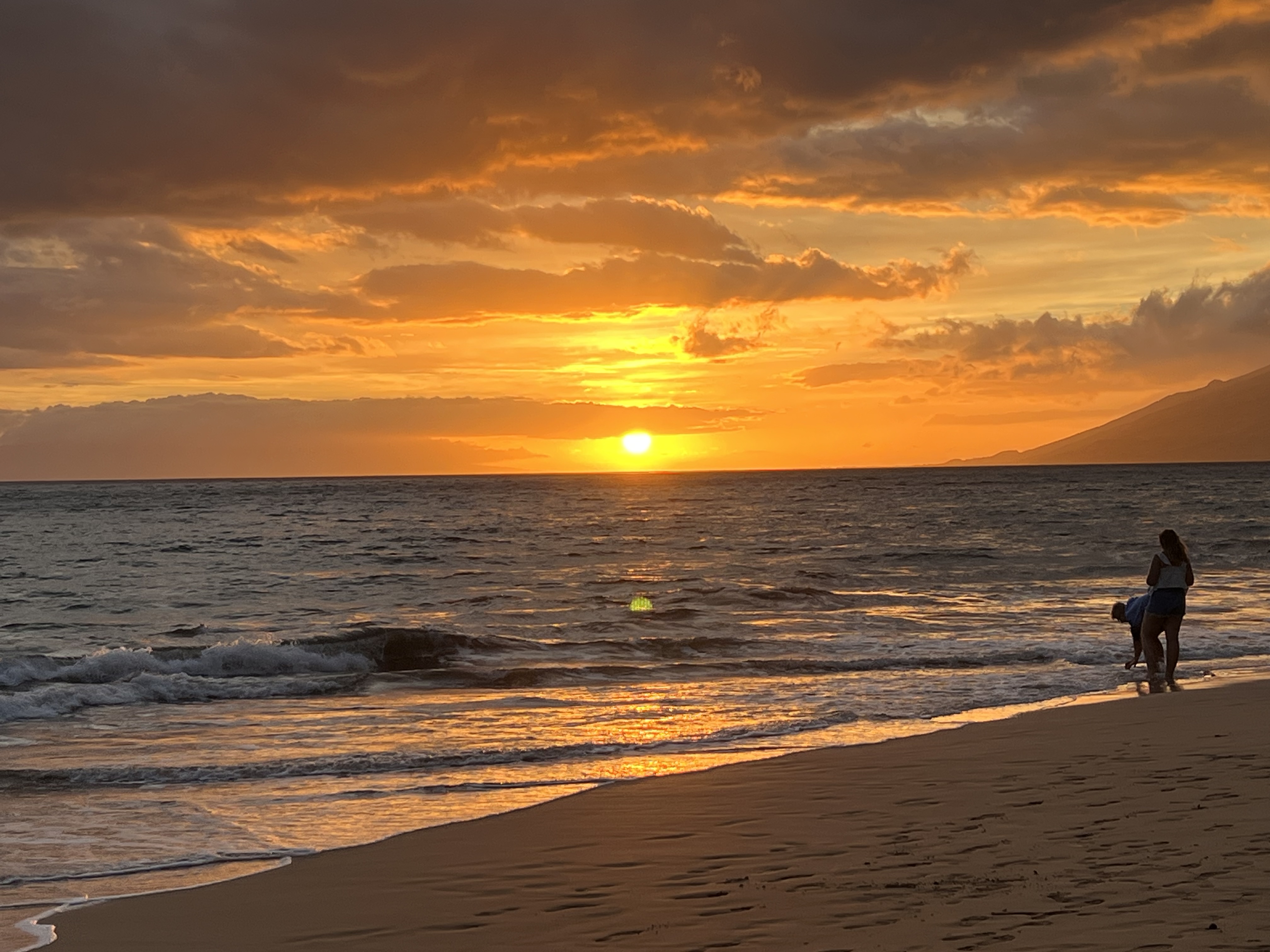 Couple silhouetted on Kama'ole Beach at sunset — golden light, Lānaʻi on the horizon, June 2026