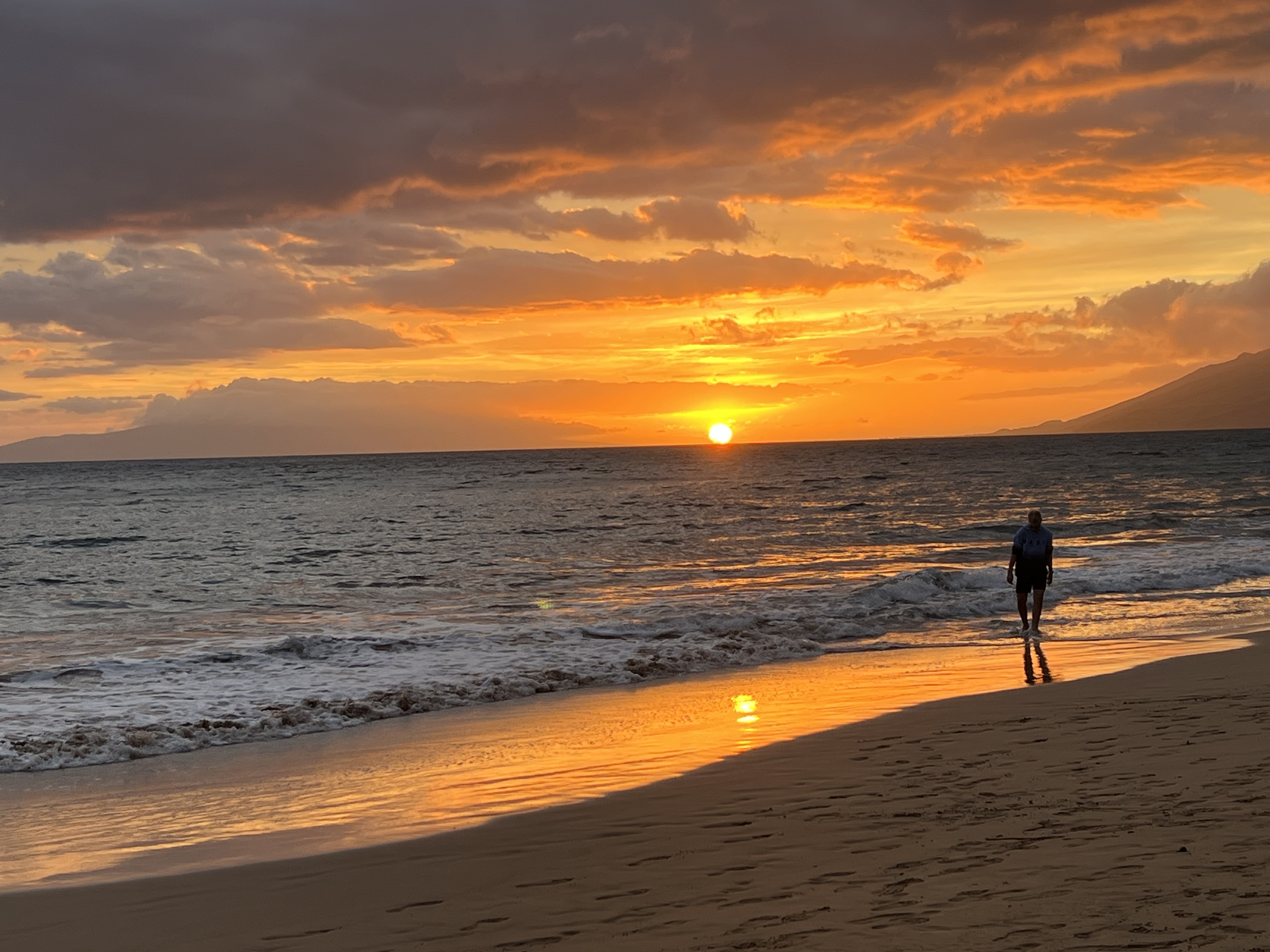 Person walking along Kama'ole Beach at sunset — golden light on the water, June 29, 2026