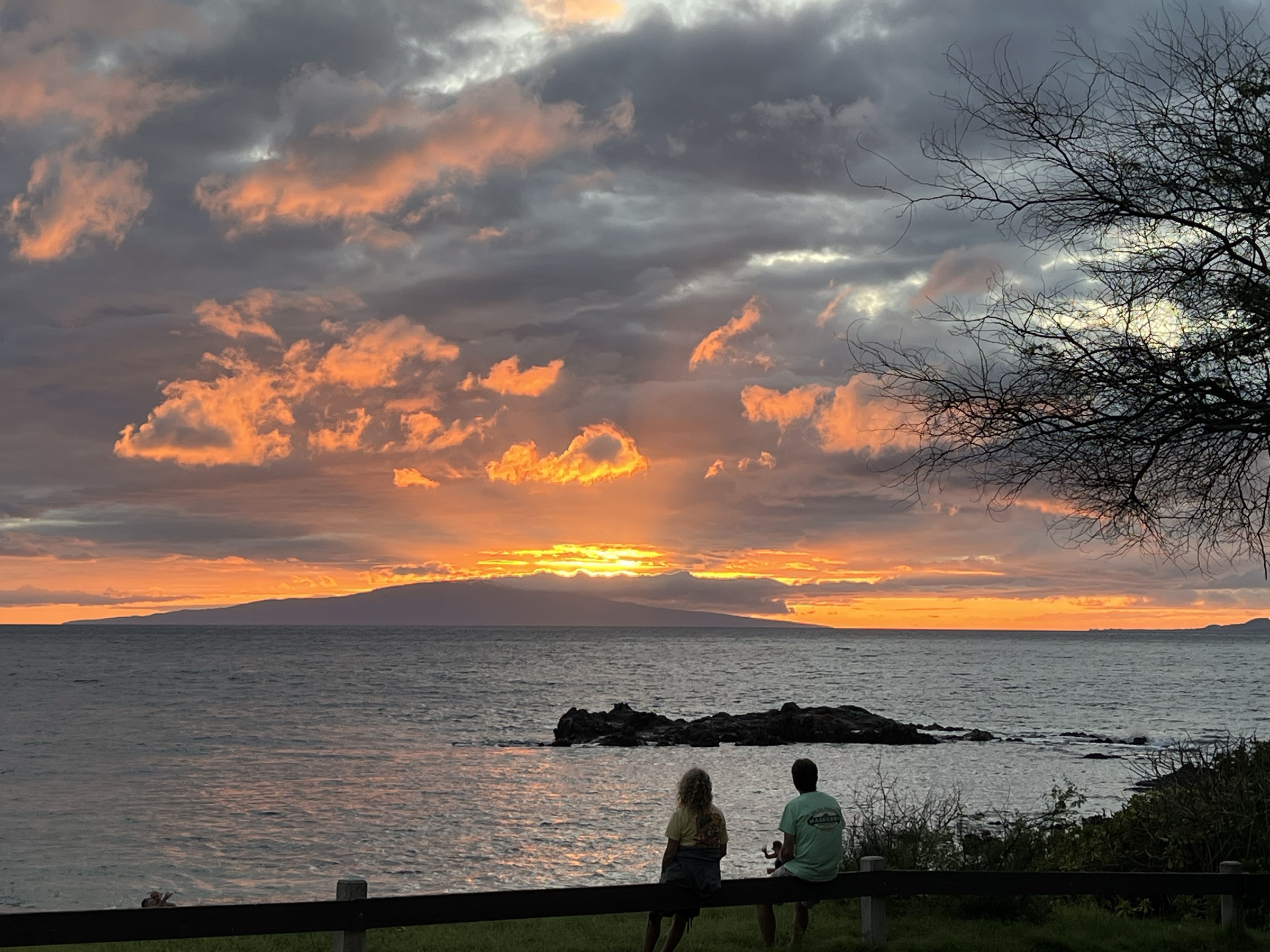 Couple on a bench watching the sun set over the West Maui mountains