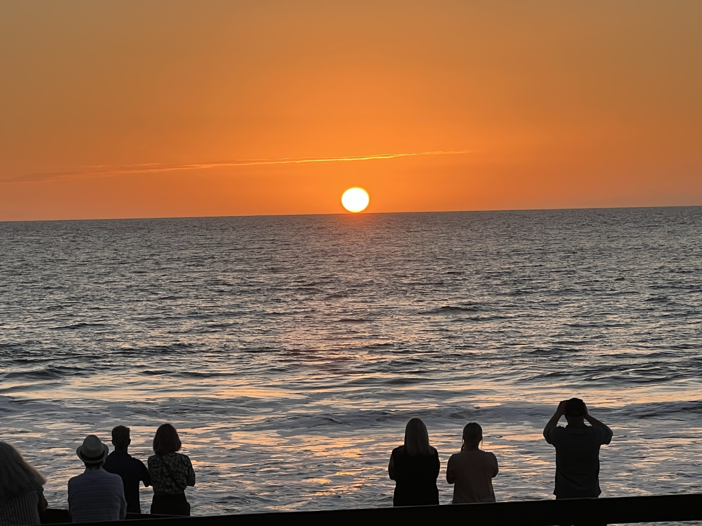 Group watching a brilliant orange sunset from the beach boardwalk