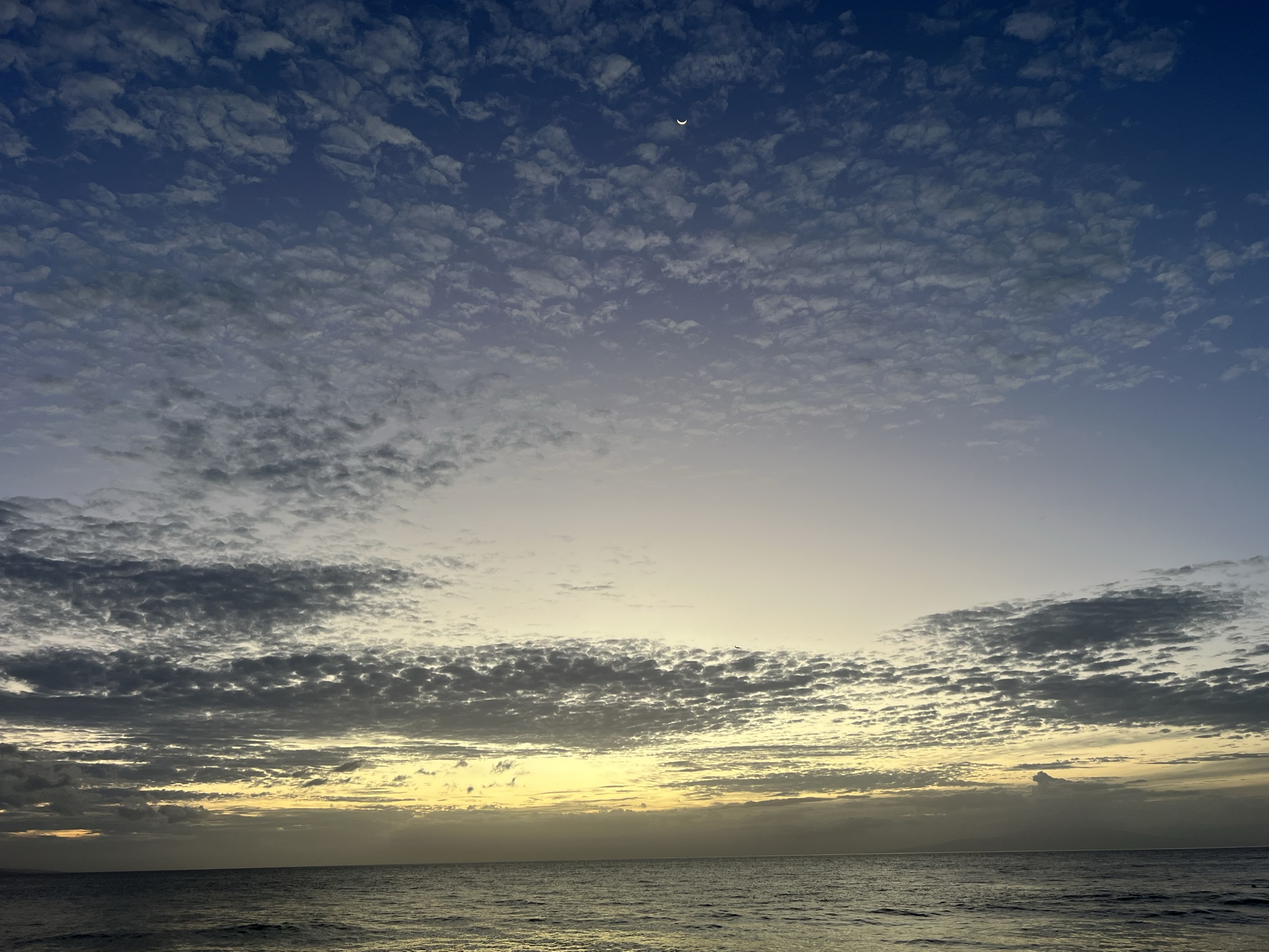 Crescent moon visible in textured cloudscape after sunset