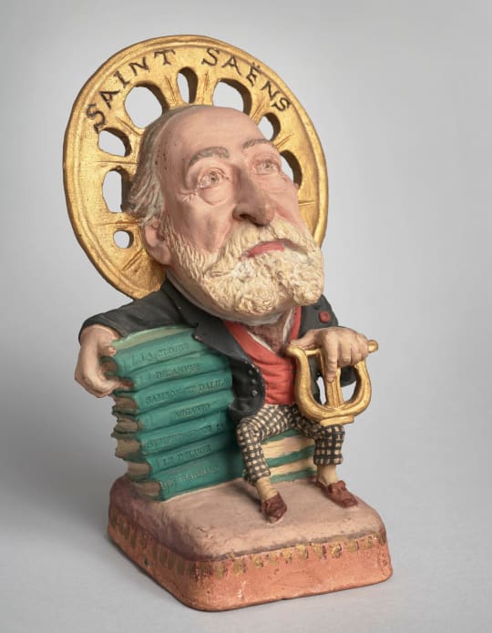 Caricature de Saint-Saëns appuyé sur les partitions de ses œuvres. Statuette en terre cuite par Kotra, après 1901. BnF, Bibliothèque-musée de l'Opéra.
