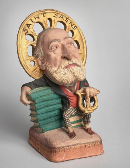 Caricature de Saint-Saëns appuyé sur les partitions de ses œuvres. Statuette en terre cuite par Kotra, après 1901. BnF, Bibliothèque-musée de l'Opéra.
