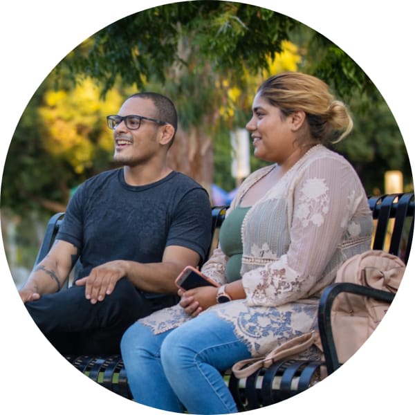 Photo of Oportun customer sitting on a park bench with a friend after getting a loan approved
