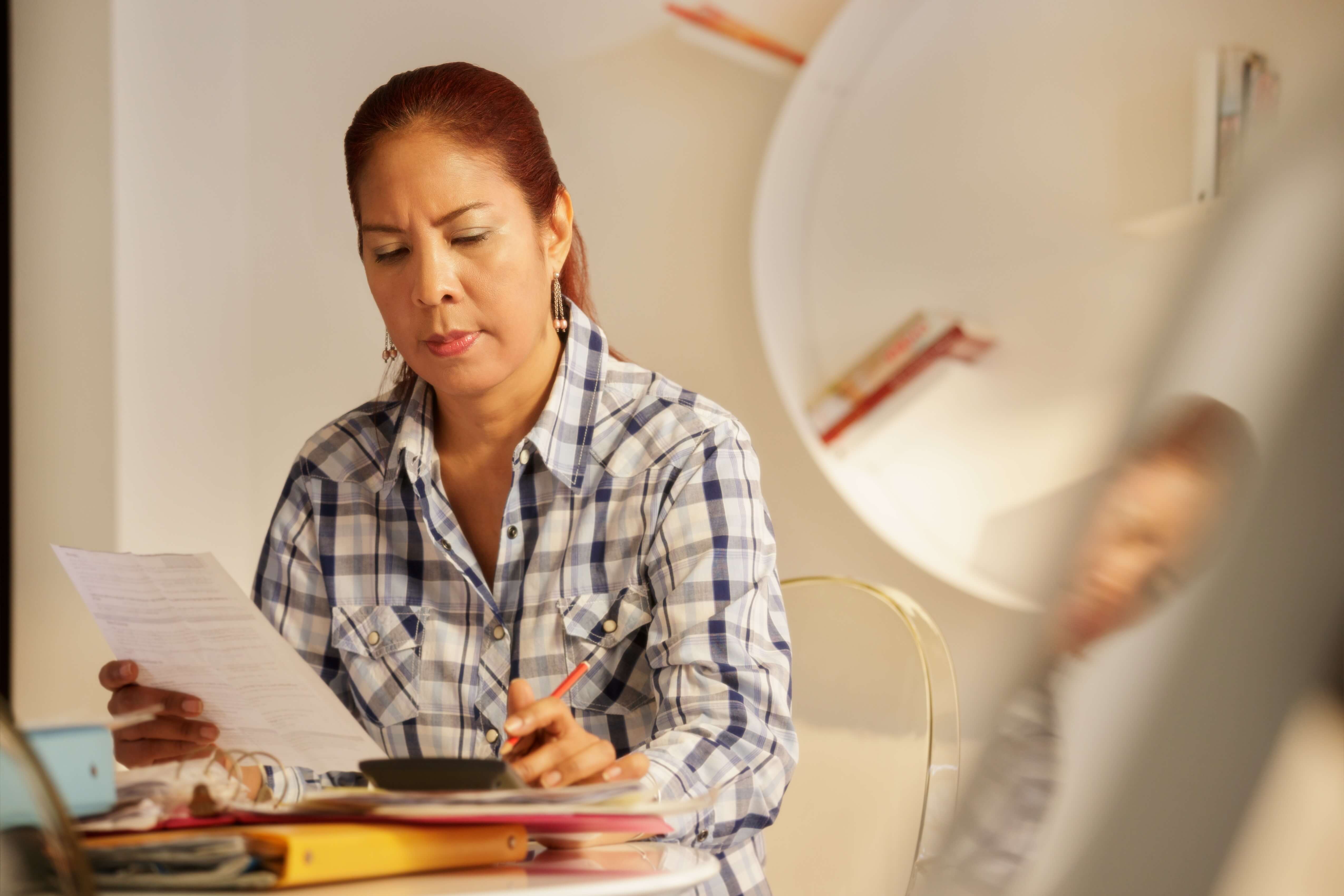 Photo fo a woman at her table trying to work out her tax returns