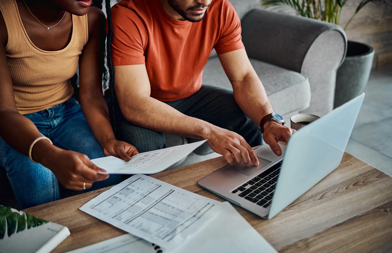 Couple reviewing paperwork and cross referencing the documents with information non their computer.