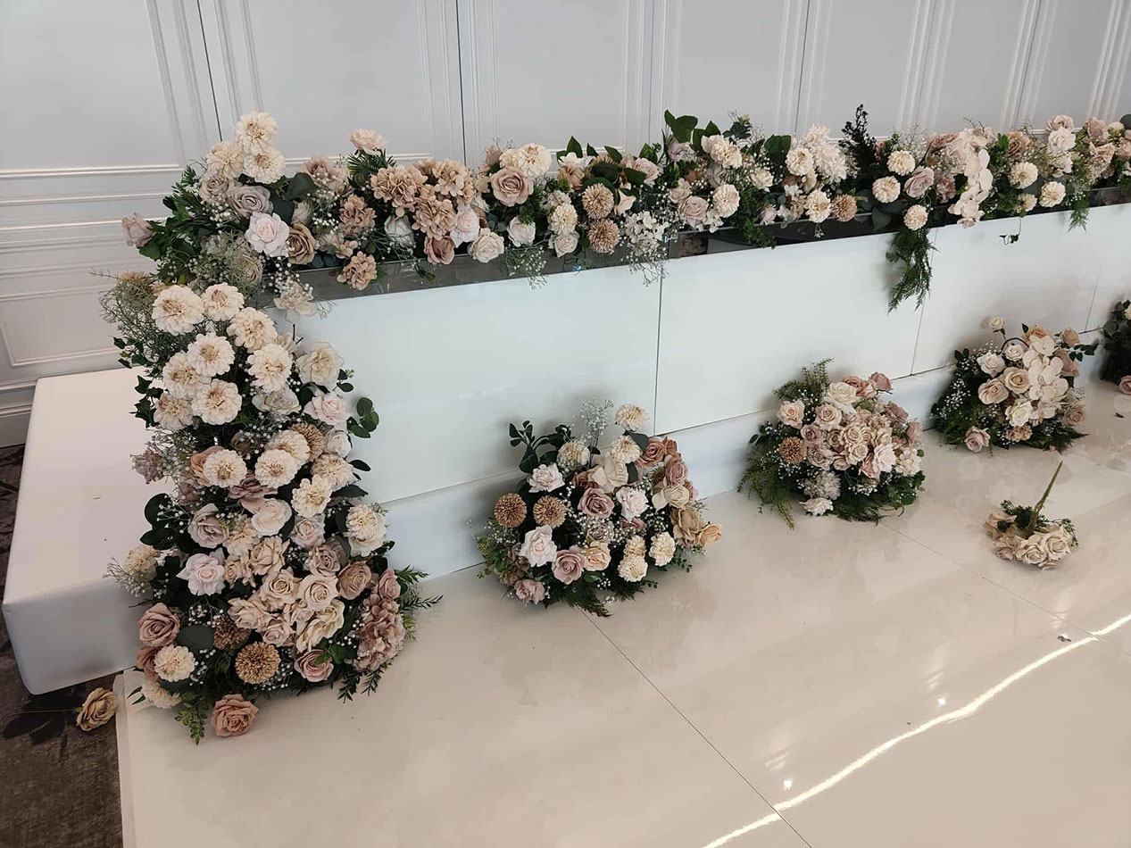 Gloss bridal table decorated with cascading ivory, blush, and champagne-toned floral arrangements, styled against a white backdrop for a wedding reception.