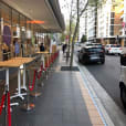 A sidewalk with tables and chairs in front of a building, offering a charming outdoor seating arrangement.