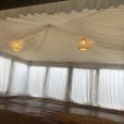 A white tent with white curtains and a wooden floor illuminated by a white pendant rope light.