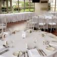 A room with white round banquet tables and chairs set up for a wedding.