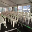 A row of stackable white plastic chairs available for hire in a tent.